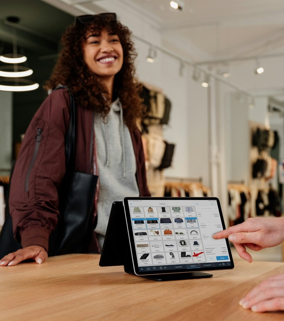 A shopper at a store counter while staff ring up the order on a point-of-sale tablet